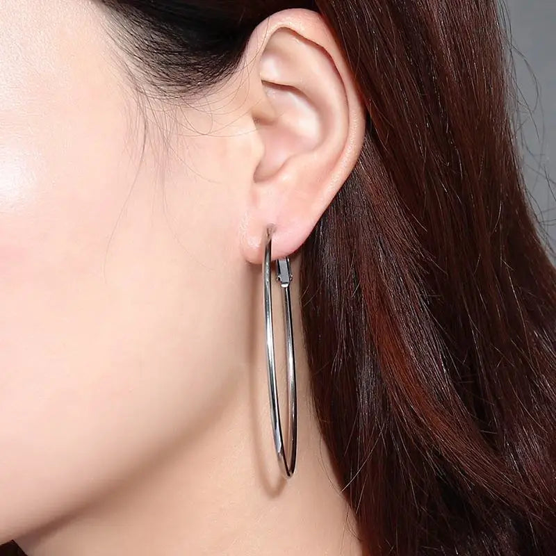 Silver-tone stainless steel hoop earring shown worn, with a large, slim oval loop.