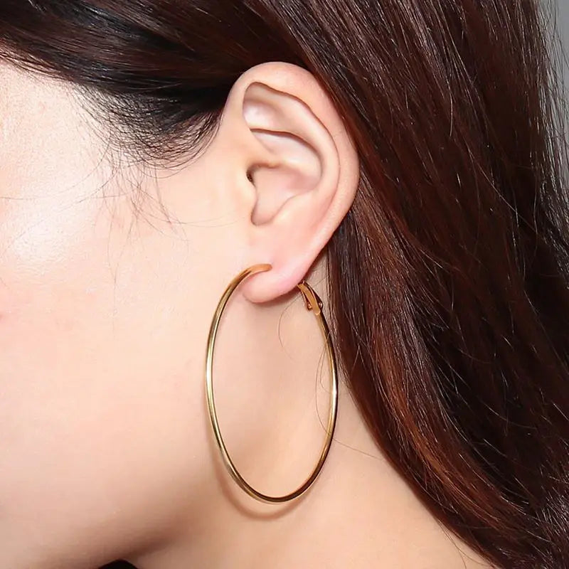 Gold-tone stainless steel hoop earring shown worn, with a large, slim oval loop.