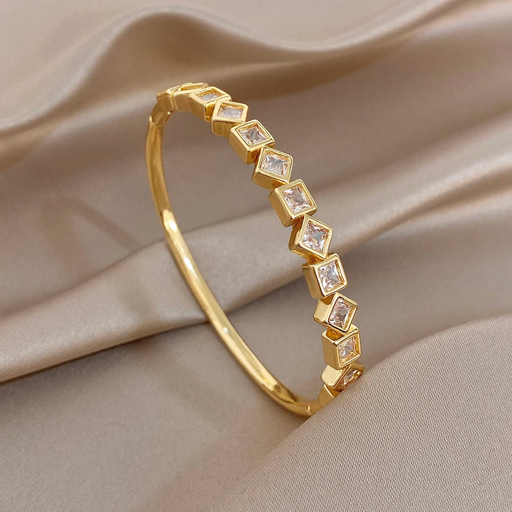 Gold-plated cuff bangle with repeating square zirconia link accents along the band