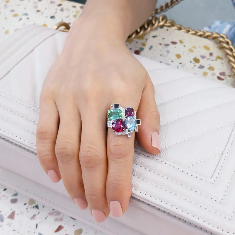 Two-tone gemstone ring worn on a finger, with colorful stones and clear accents