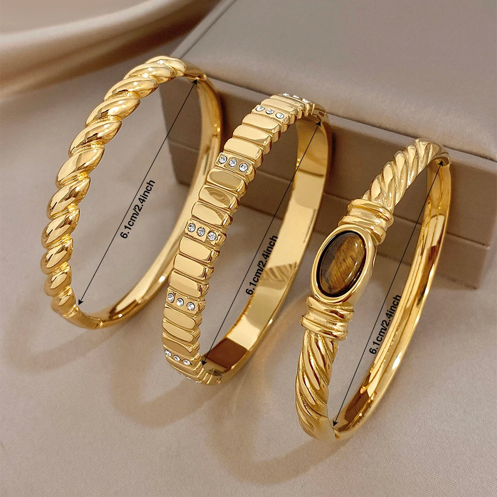 Gold-tone cuff bangles with textured twist, oval stone, and rhinestone detailing