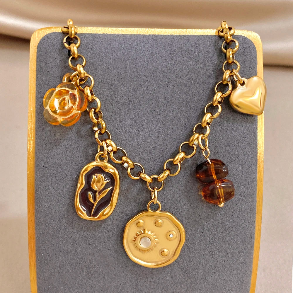 Gold tone charm bracelet featuring rose, leaf, coin-like tag, heart, and amber beads