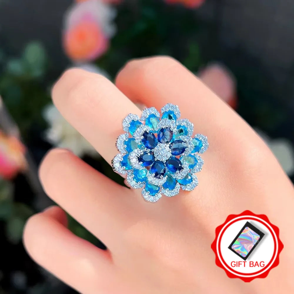 Blue layered flower ring shown on a hand; gift bag included
