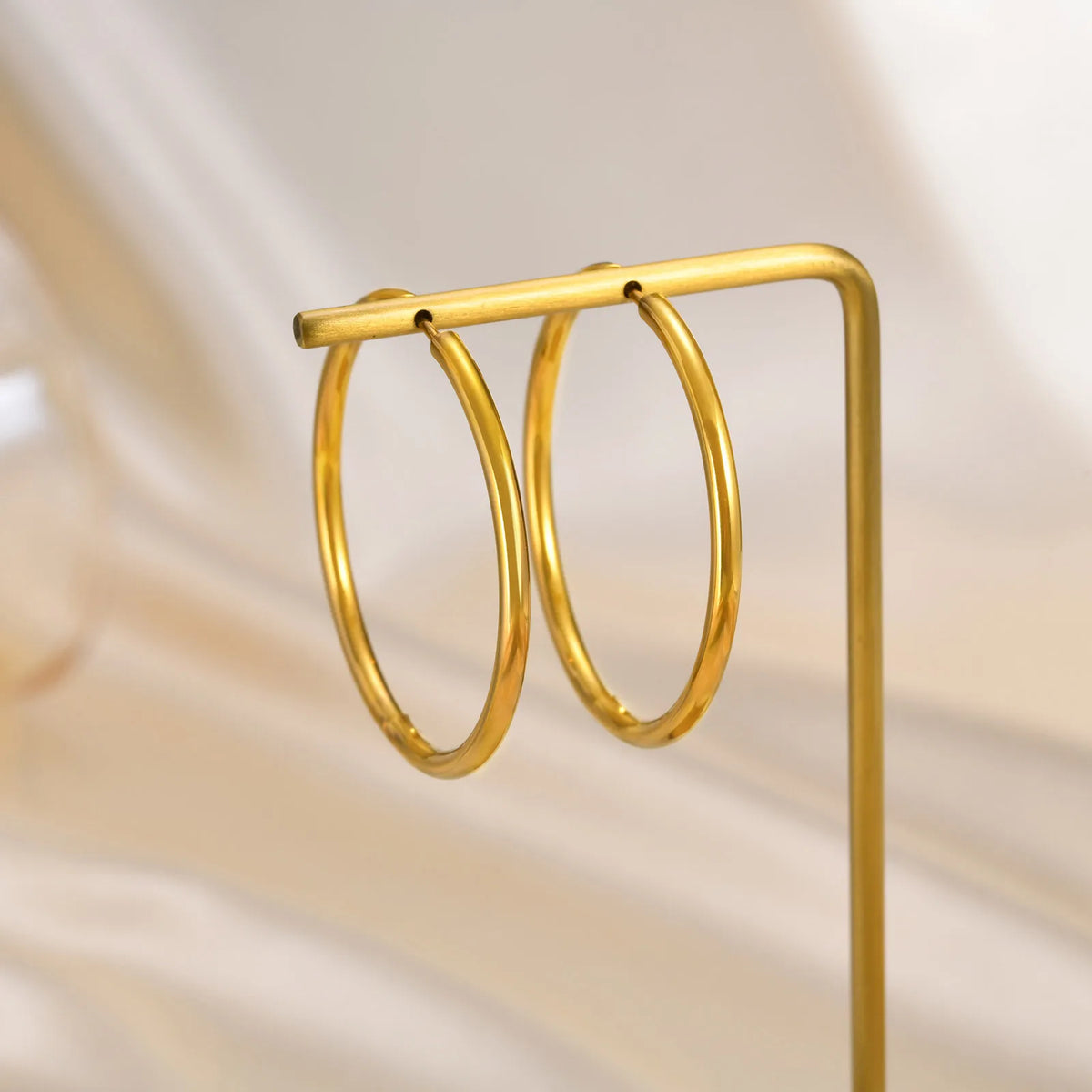 Pair of slim gold hoop earrings hanging from a display stand.