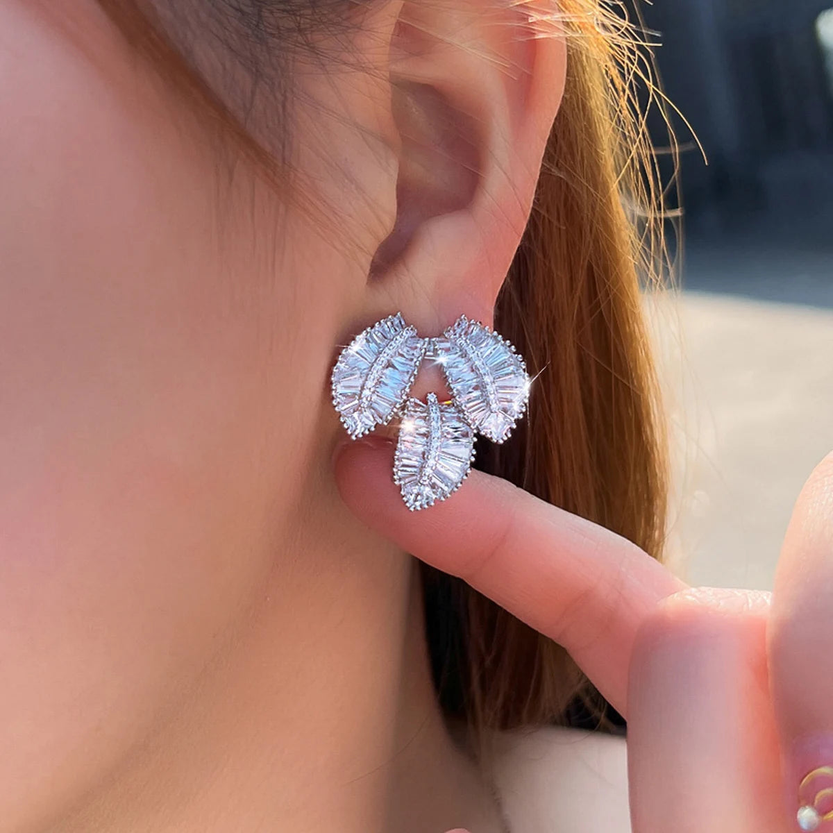 Silver-tone cubic zirconia leaf earrings worn on an ear, with three clustered leaf-shaped stones.