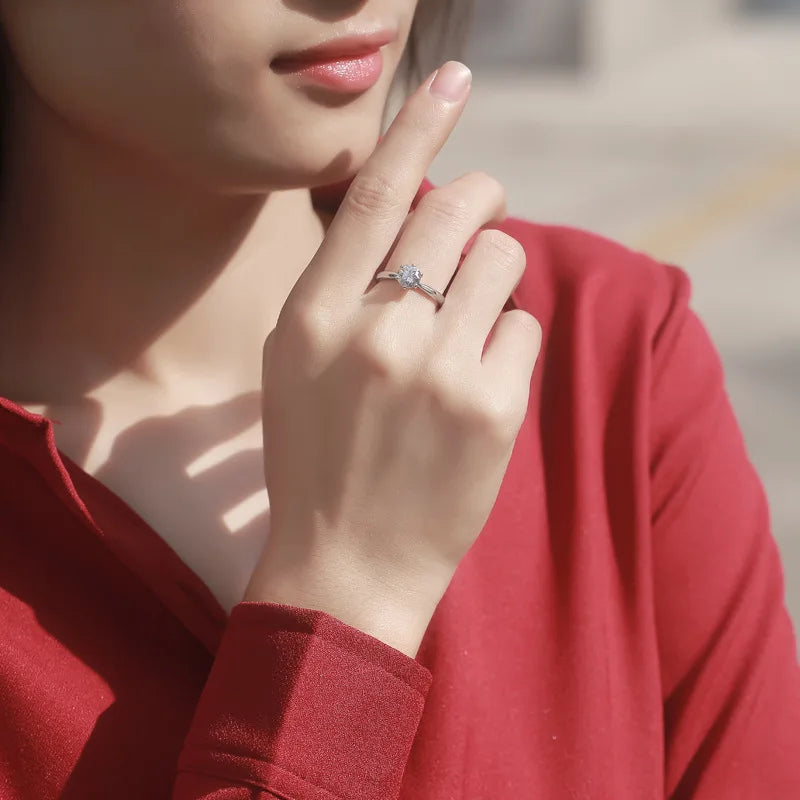Silver-tone six-prong round cubic zirconia ring on woman's finger, red sleeve