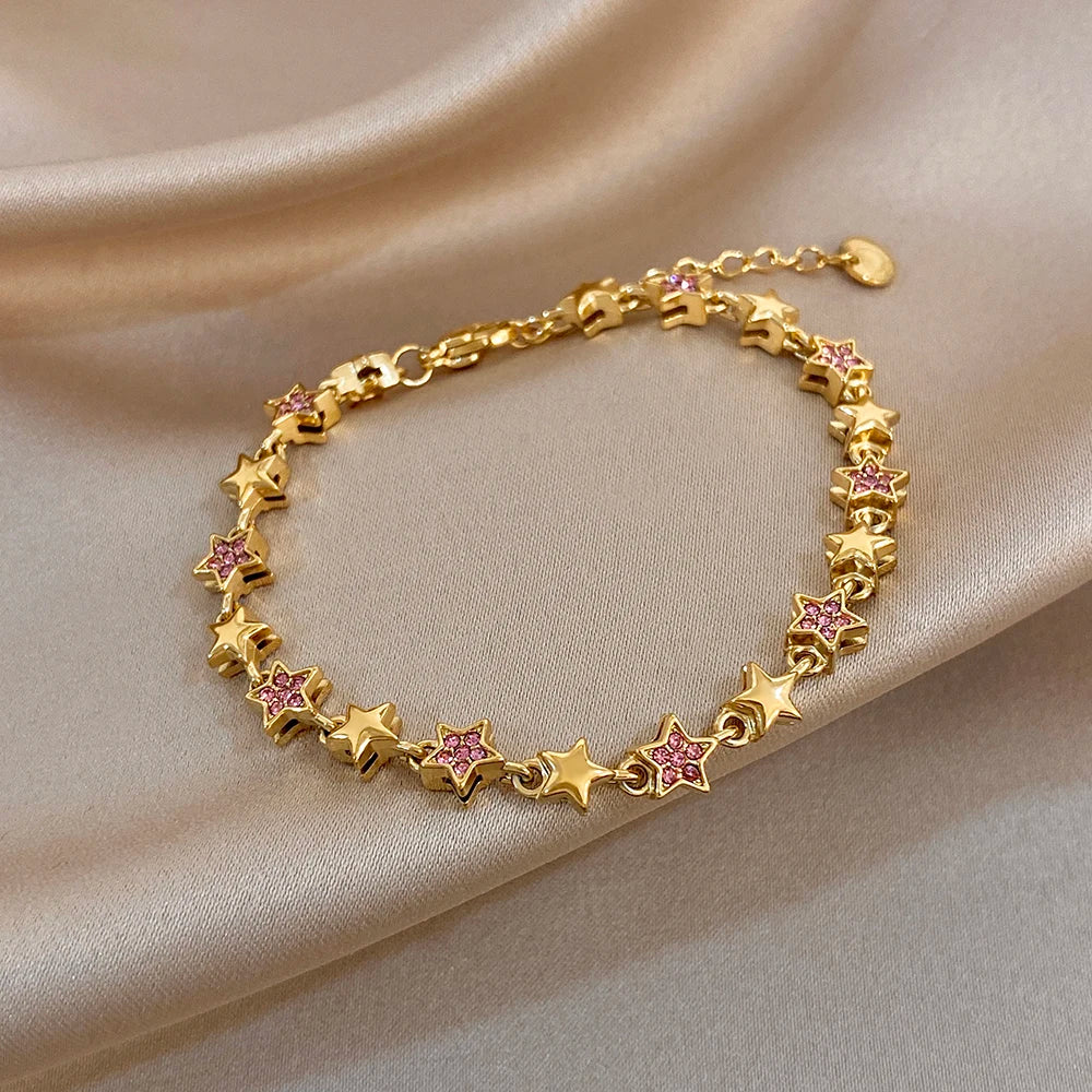 Gold-tone star charm bracelet with pink and white gem accents, round bezel links