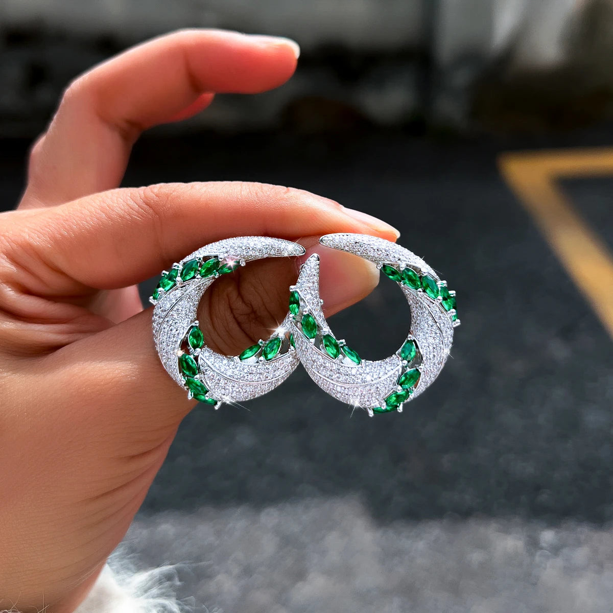 Green and white cubic zirconia crescent drop earrings held in hand