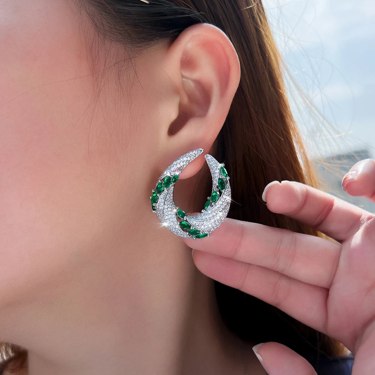 Green and white cubic zirconia crescent earring worn on the ear, shown in close-up