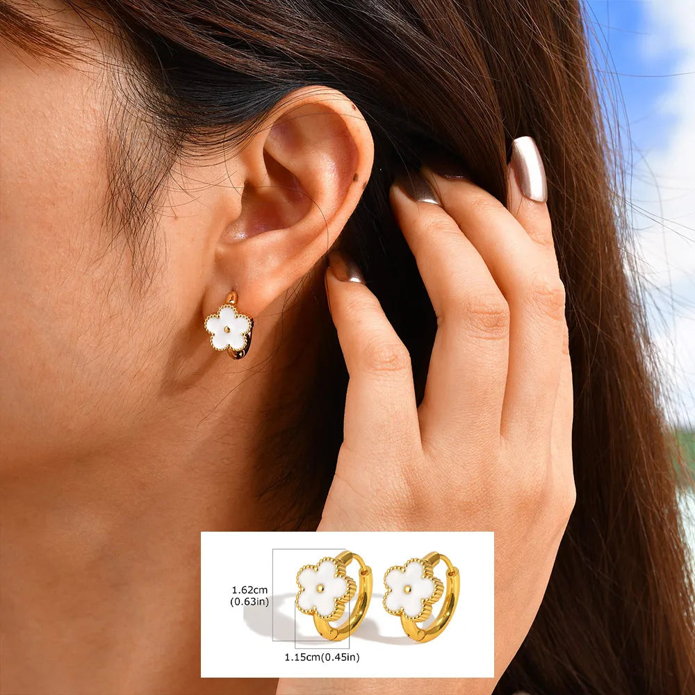 Gold-tone flower huggie earrings with white petals and dark centers.