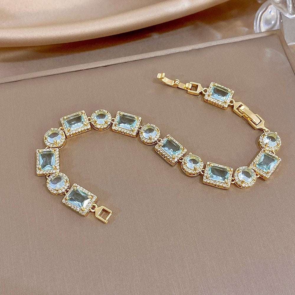 Gold-tone geometric bracelet with blue square and round crystal links, gold clasp detail