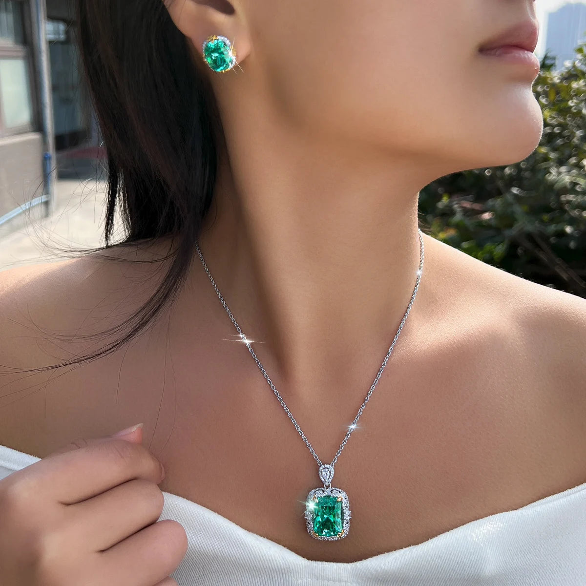 Green rectangular crystal pendant necklace and matching stud earring, worn close up