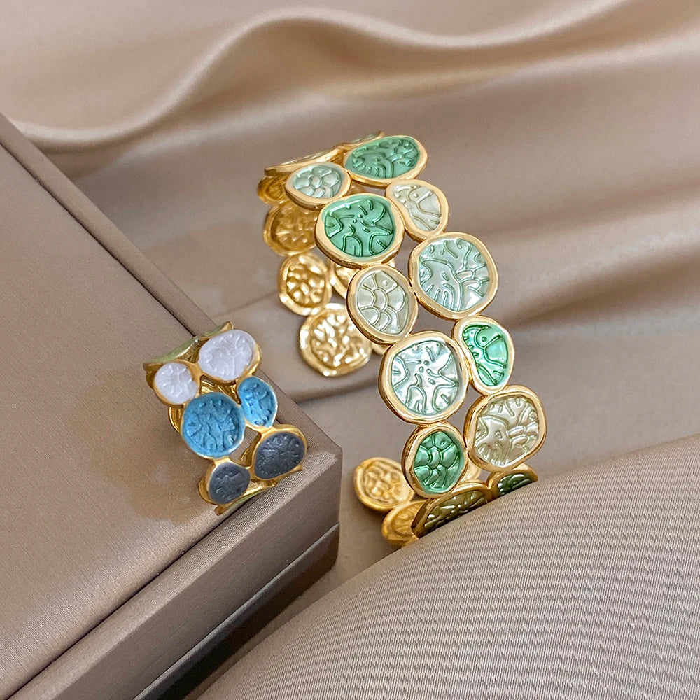 Gold-tone open cuff bracelet with green and light enamel leaf coin patchwork accents