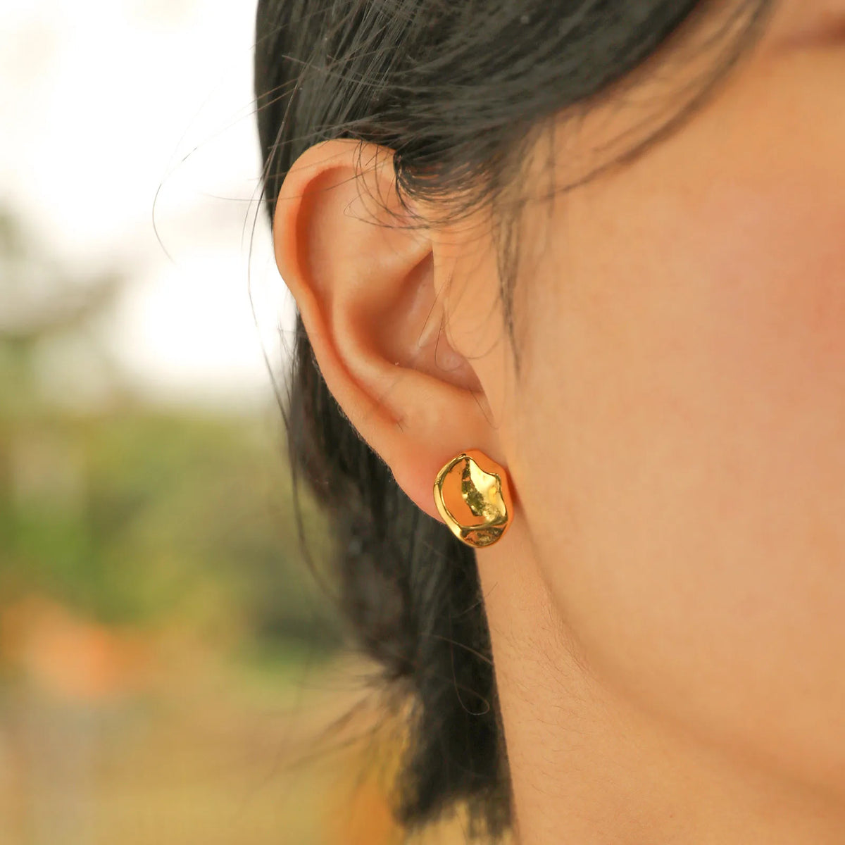 Geometric gold-tone stud earrings on ear, rounded faceted front