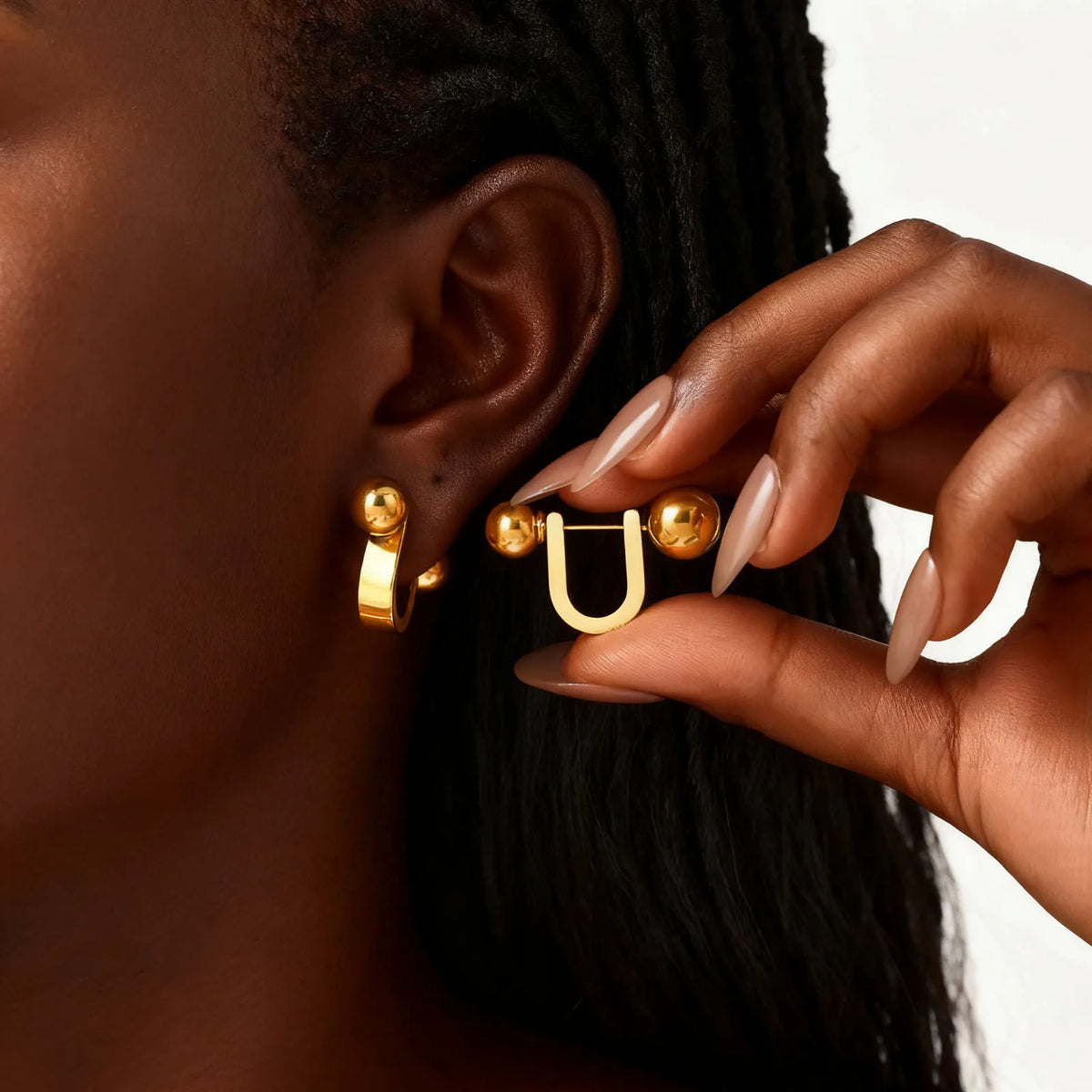 Gold U-shaped hoop earring with ball ends shown beside the ear