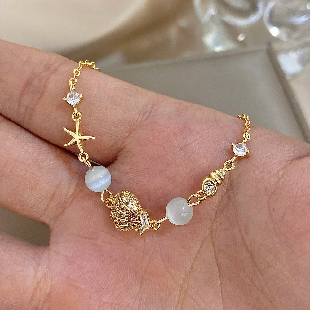 Gold-tone charm bracelet with starfish and shell charms, moonstone-style beads, rhinestones
