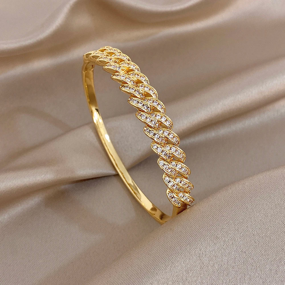 Gold tone cuff bangle with clear rhinestone marquise-style link band on the surface.