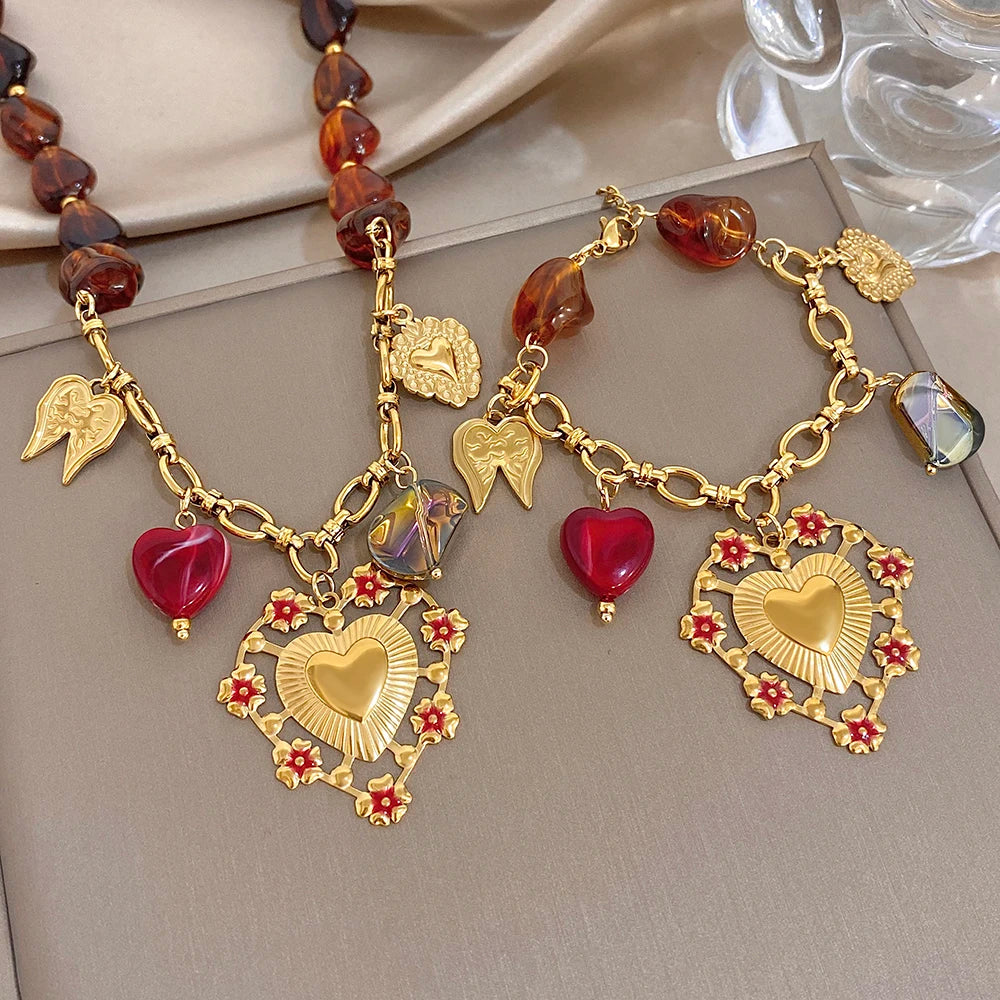 Gold-tone layered charm bracelet with red hearts, amber beads, heart pendant, and wing charms