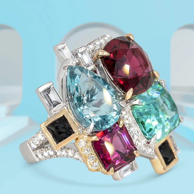 Two-tone ring featuring a blue pear-shaped stone, colorful gems, and clear accents