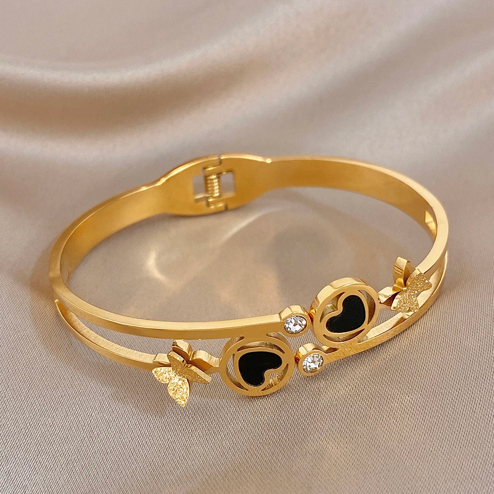 Gold-tone wide cuff bangle with black enamel heart circles, butterfly charms, and rhinestones