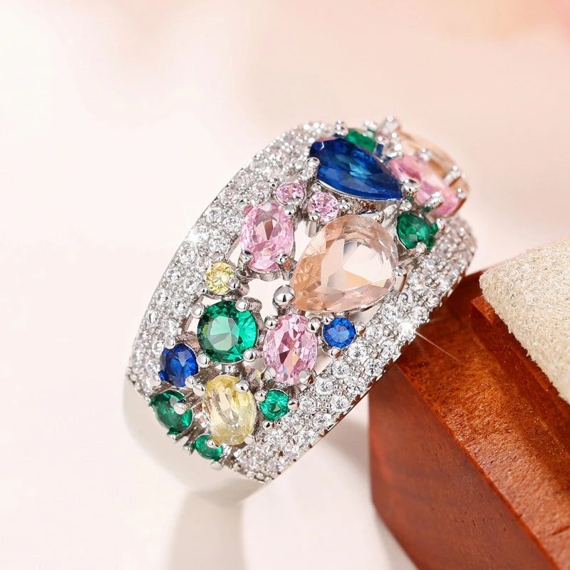 Silver-tone cubic zirconia ring with blue center stone and green accents, on a jewelry box.