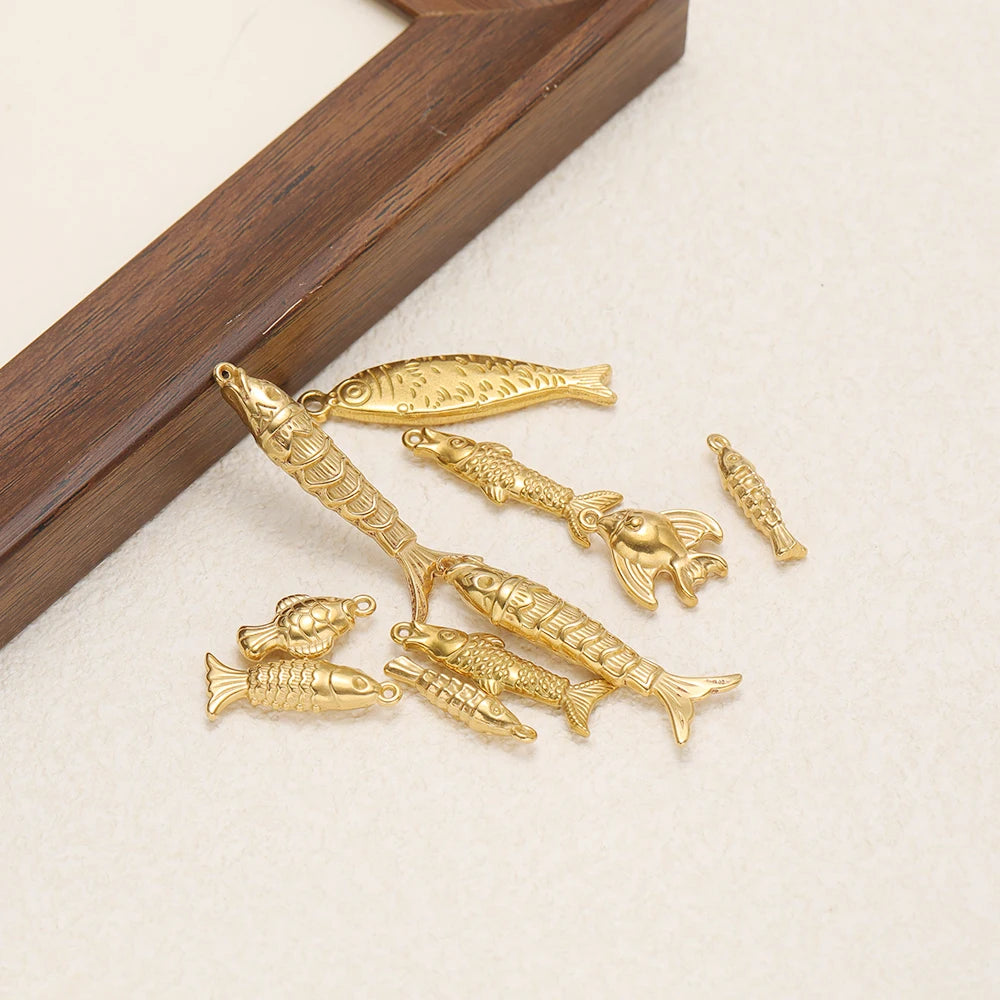 Gold-tone fish charm set with loops, scattered on a wooden surface