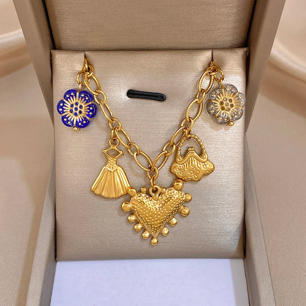 Gold chain necklace with blue flower, dress charm, and heart pendant with textured detail