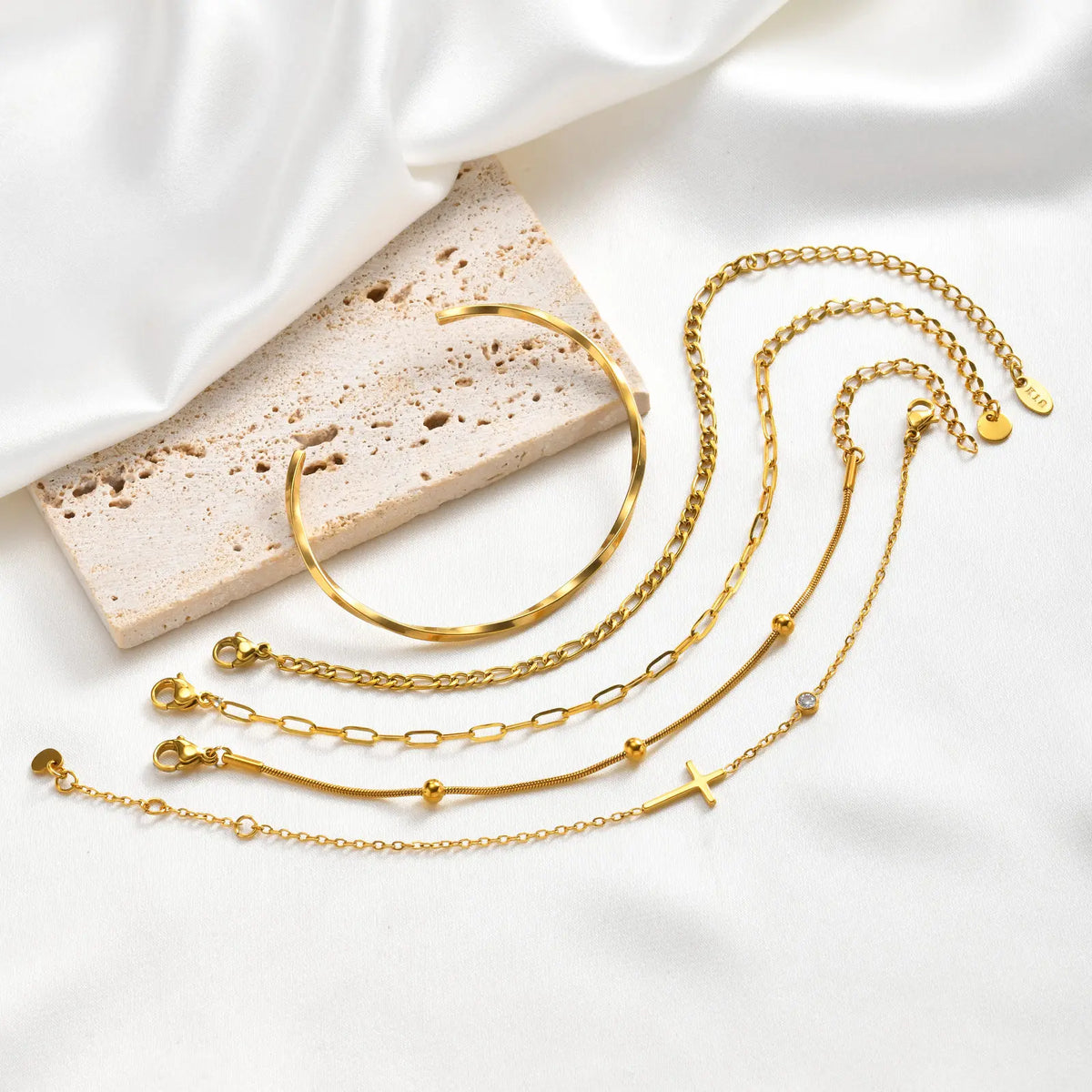 Five gold bracelets with cross charms, chain links, and cuff bangle styles