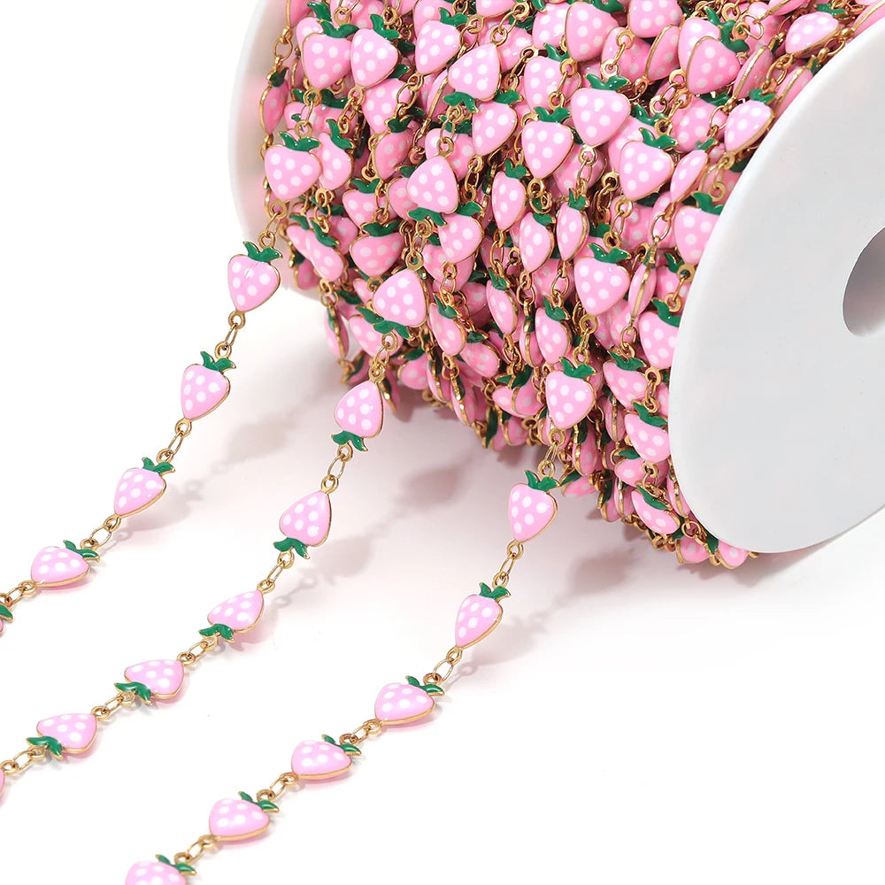 Pink enamel strawberry charm chain with gold-tone links on a spool for DIY jewelry
