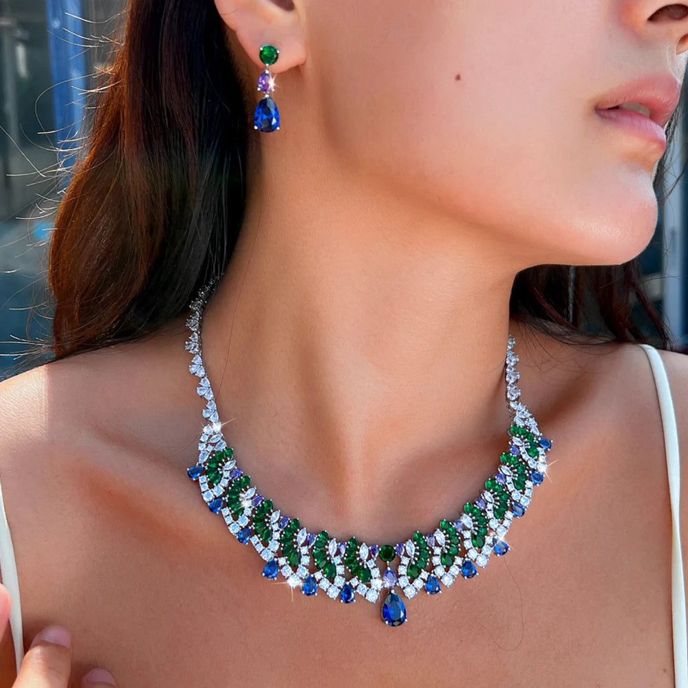 Silver-tone zircon jewelry set worn, with a green stud and blue drop earring