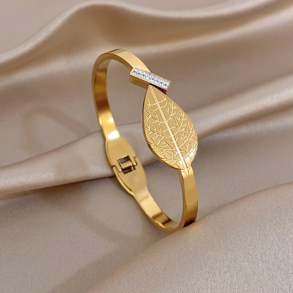 Gold leaf-pattern cuff bangle with rhinestone square accent and hinged clasp.