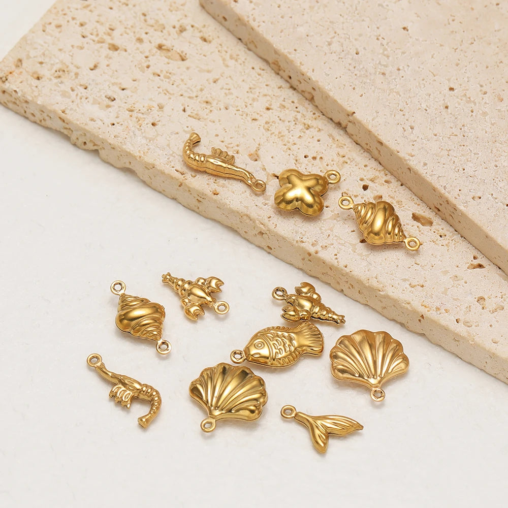 Gold hollow sea-life charm pendants with loops, scattered on light stone