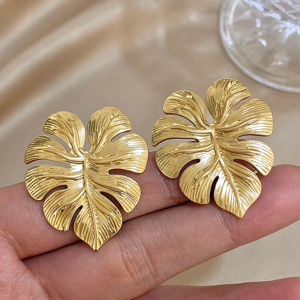 Gold leaf stud earrings shown on a hand to show their scale