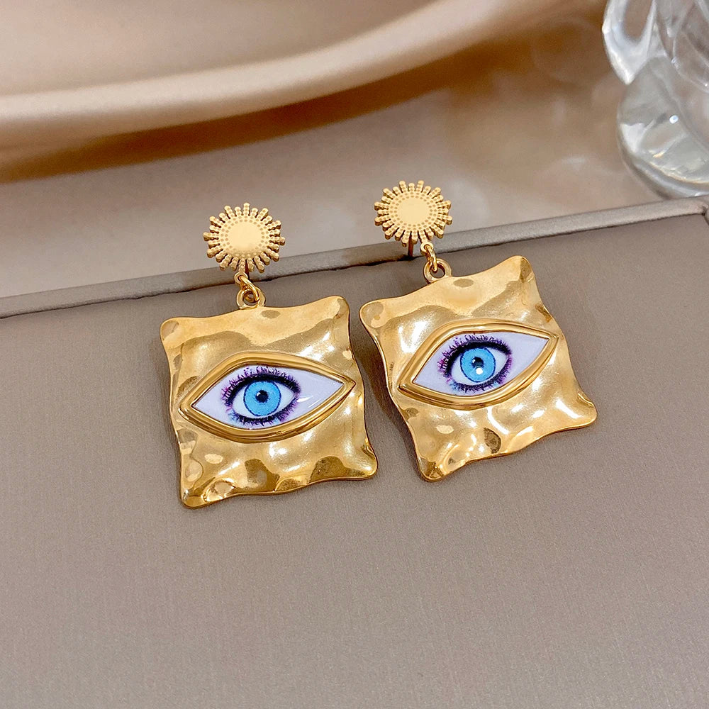Gold-tone hammered square earrings with blue evil-eye motif and round sunburst caps