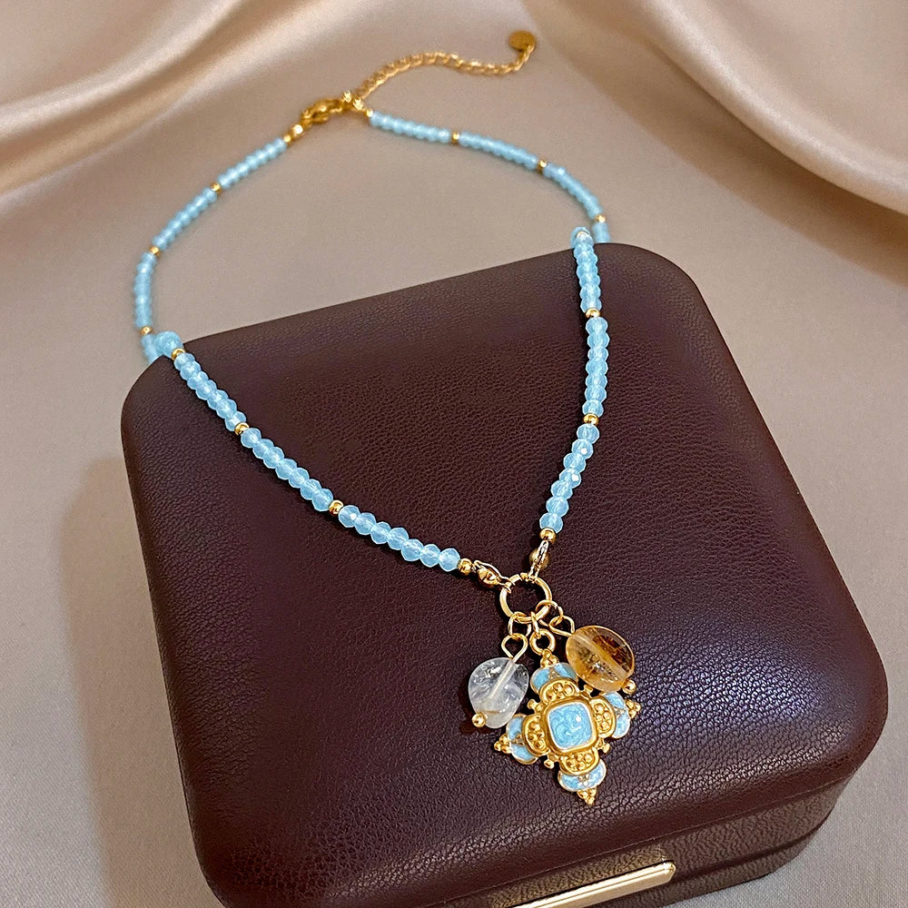 Gold-tone cross pendant necklace with clear crystal drops on a light blue beaded chain