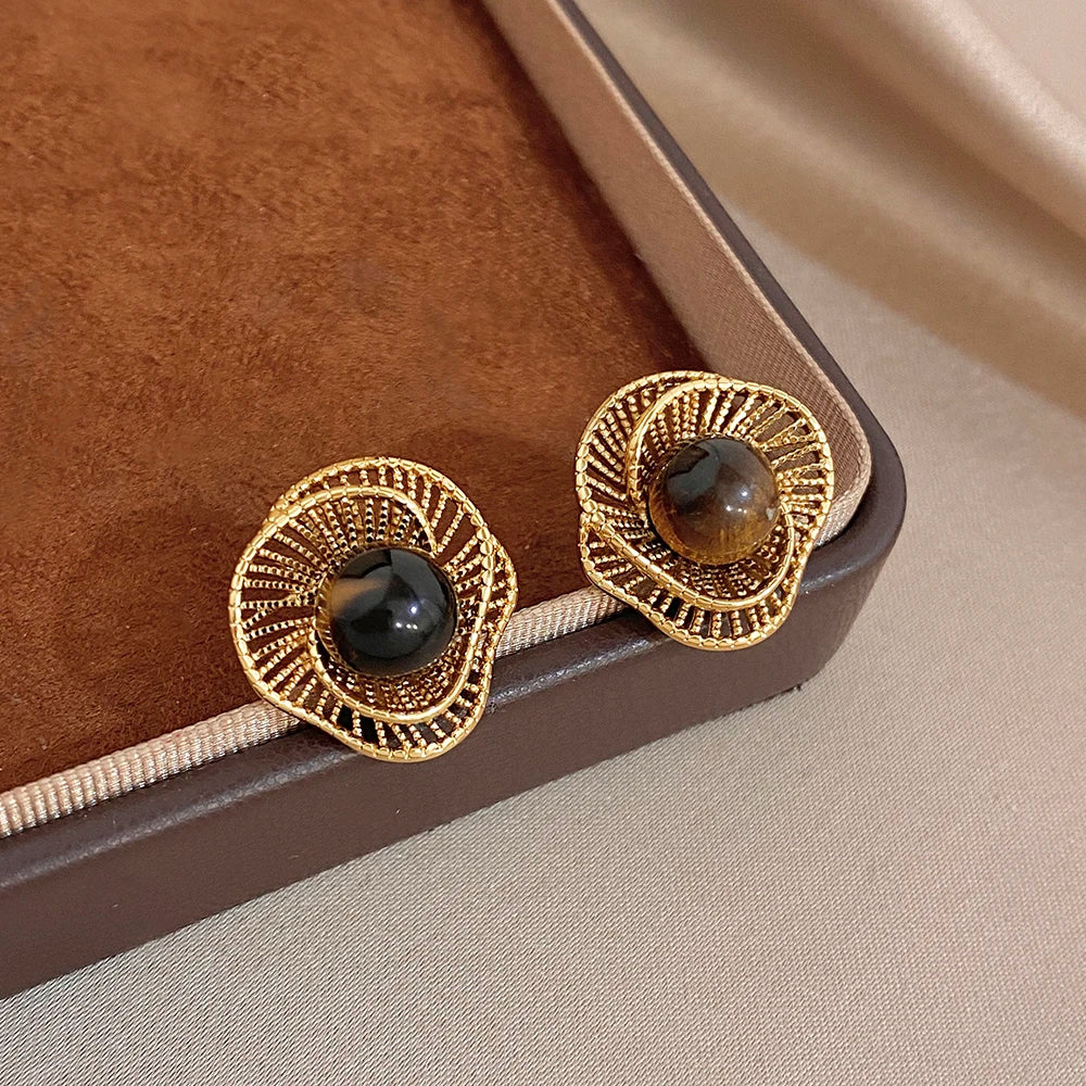 Gold-tone flower stud earrings with dark round cabochon and braided ring detail