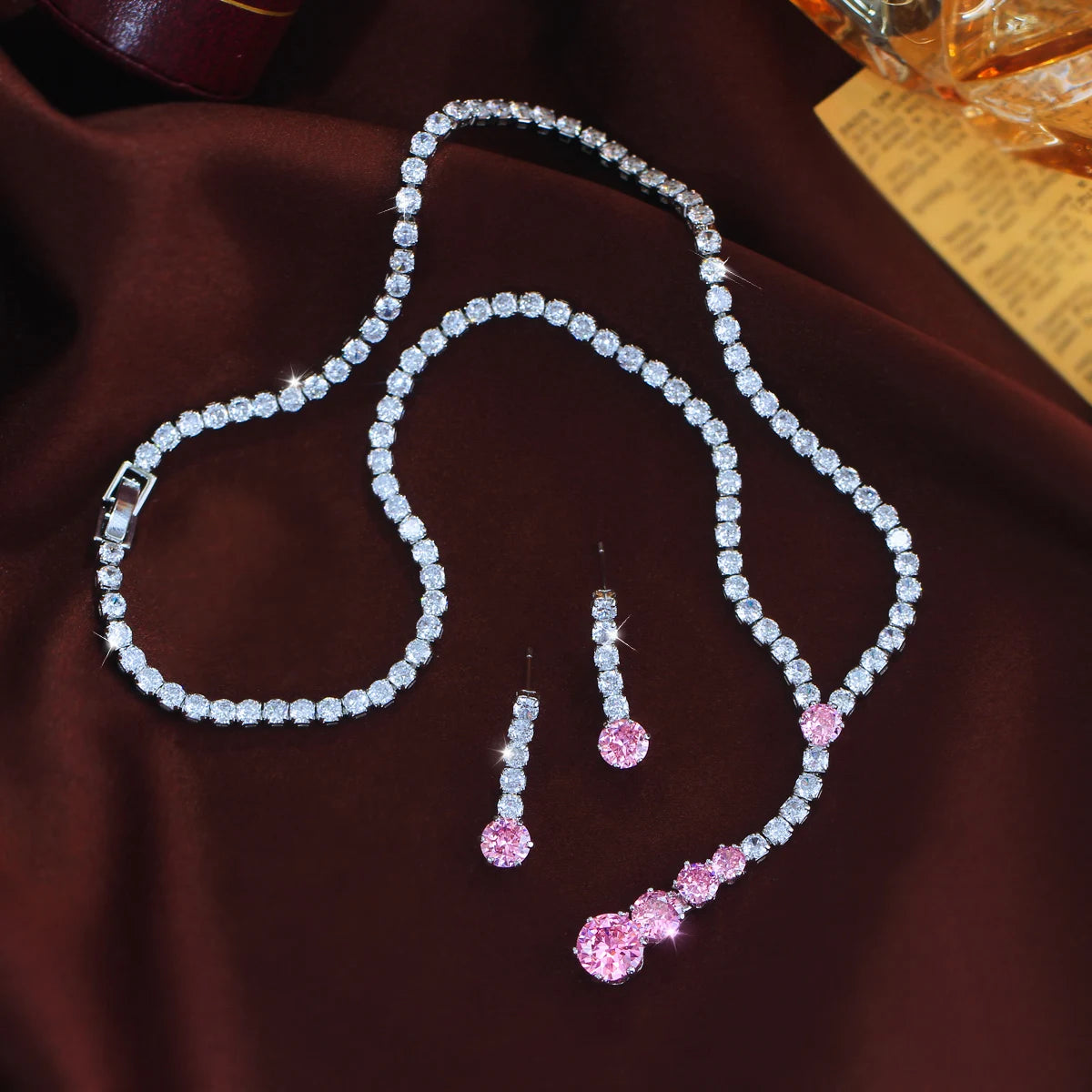Cubic zirconia necklace and earrings arranged flat, with clear stones and pink accents