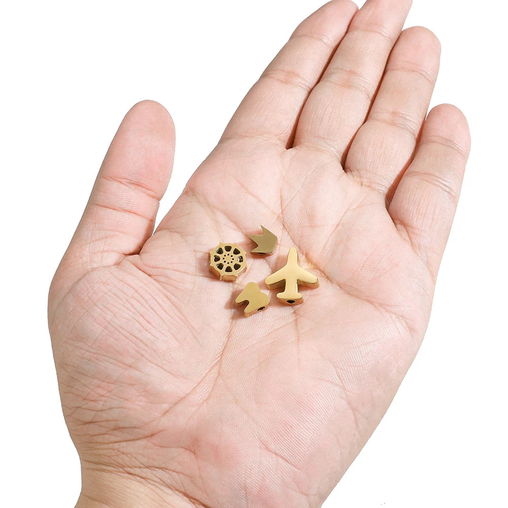 Gold-tone stainless steel spacer beads held in palm, assorted animal and symbol shapes