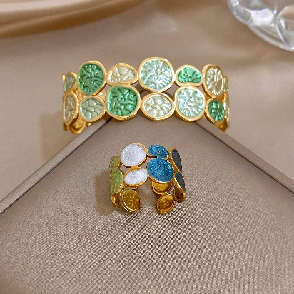 Gold-tone open cuff bracelet with green leaf enamel coins and blue enamel petal accents