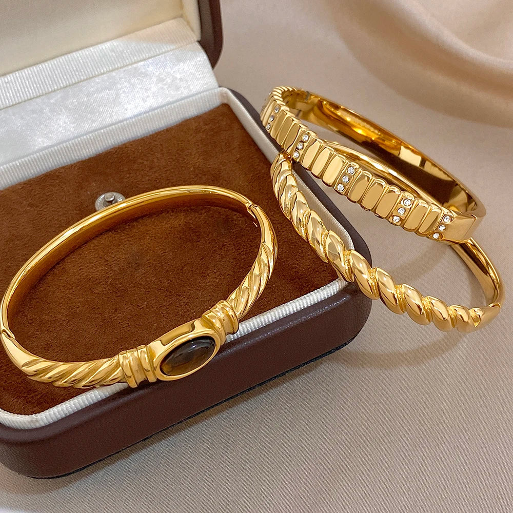 Gold-tone cuff bangles in box: twisted style with oval dark stone and crystals