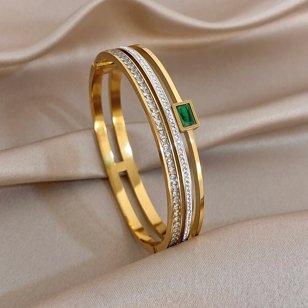 Gold-tone slim wide bangle bracelet with clear stone rows and a green square centerpiece