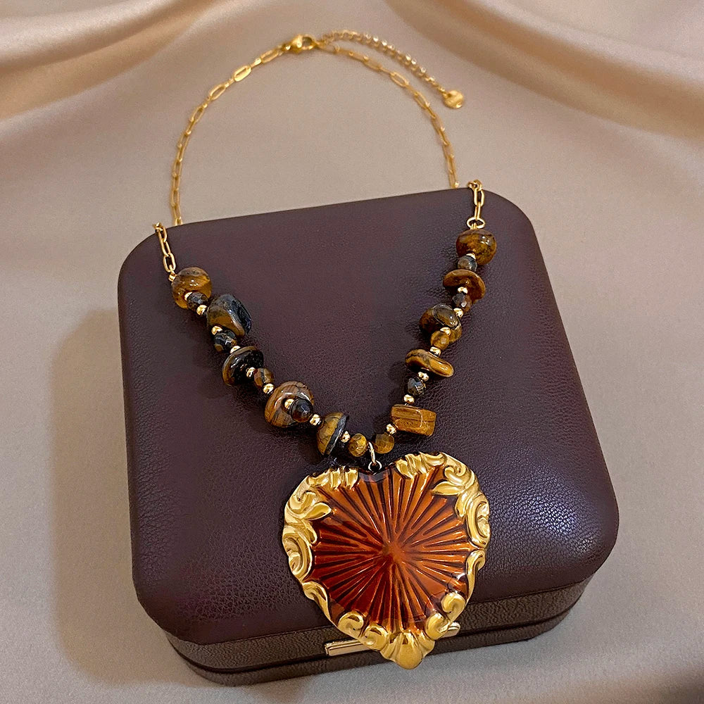 Gold heart pendant necklace with brown and black bead strand and red sunburst charm