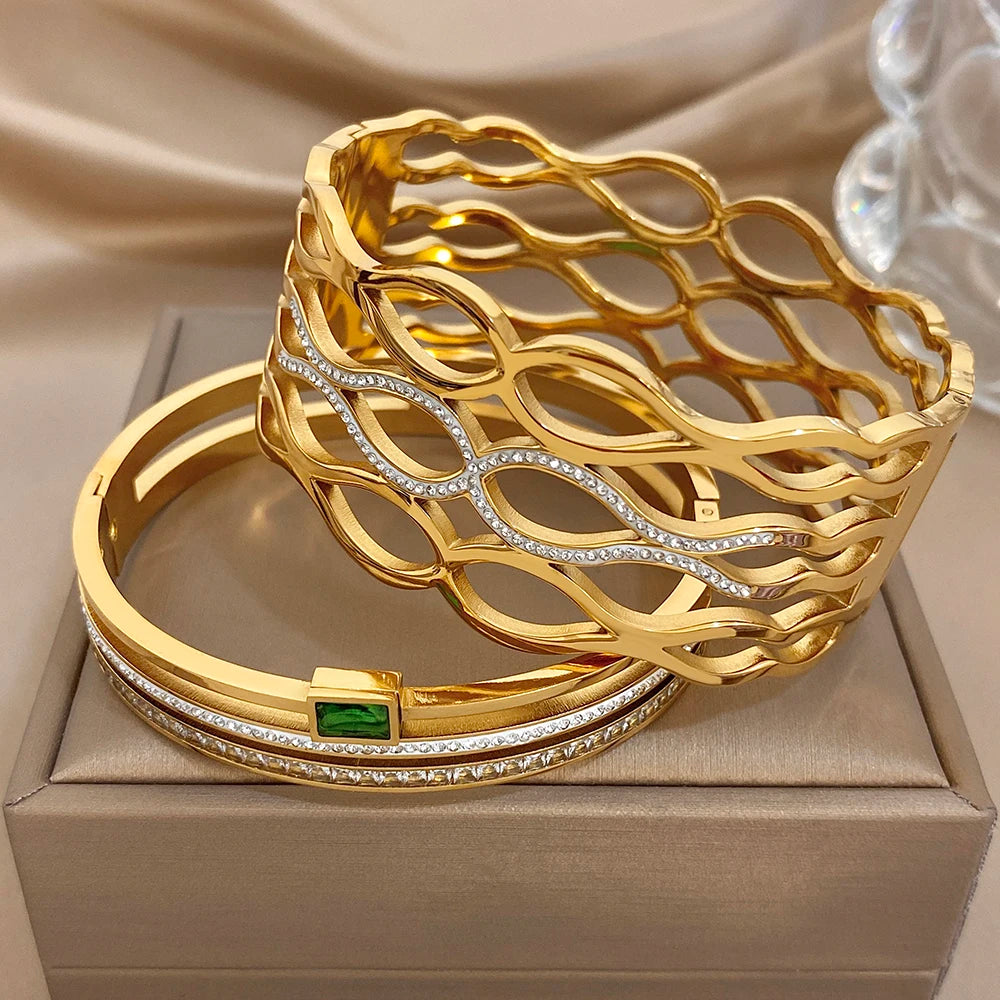 Stacked gold-tone bracelets set with oval-cut stones, chain links, and green square accents