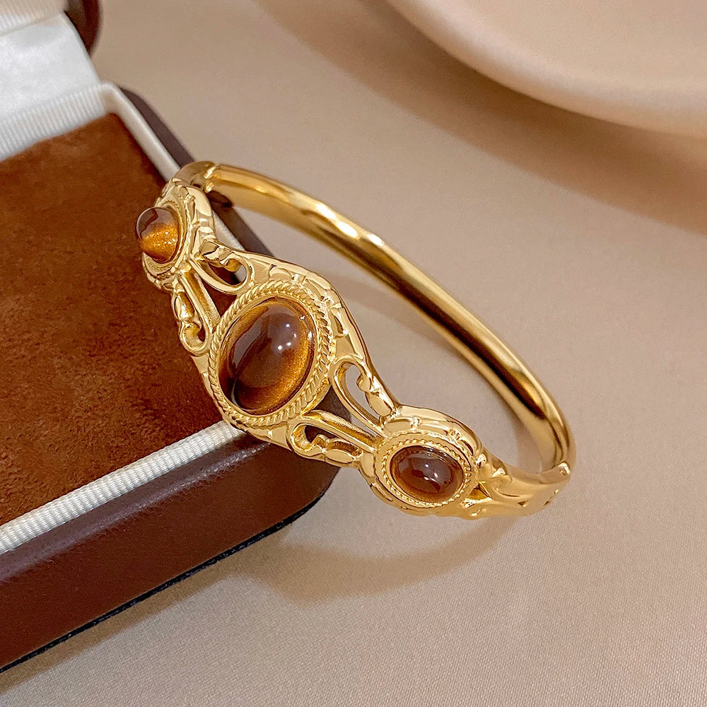 Gold-tone cuff bangle with brown oval tiger-eye stones and decorative filigree
