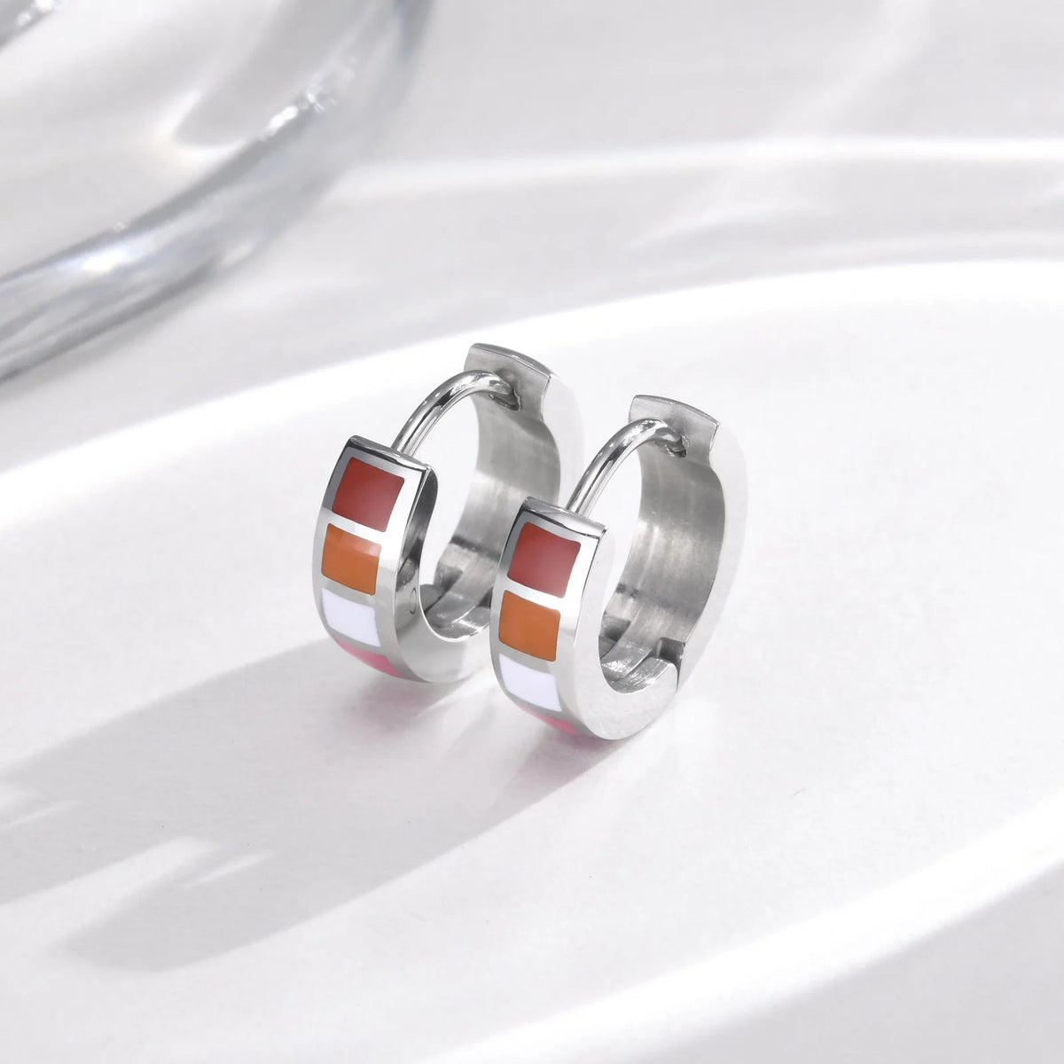Pair of stainless steel hinged hoops with red, orange, white, and magenta enamel stripes