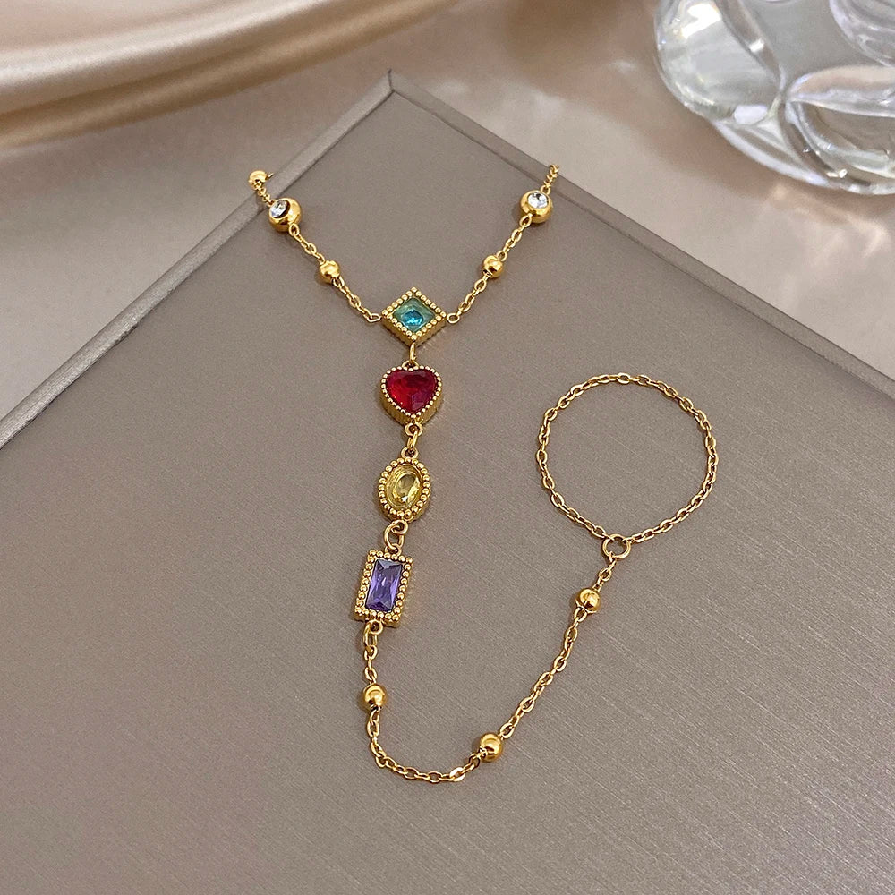 Gold-tone charm bracelet featuring blue, red heart and purple square gemstone charms