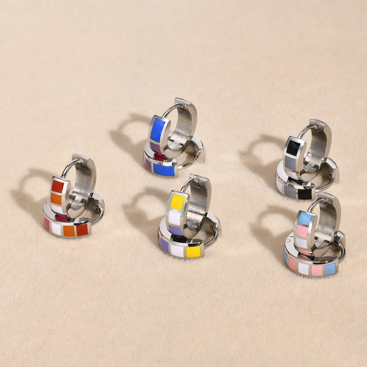 Five pairs of stainless steel rainbow enamel huggie hoops in assorted color patterns