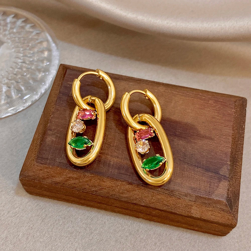 Gold geometric hoop earrings with multicolor gemstone teardrop accents on wooden display