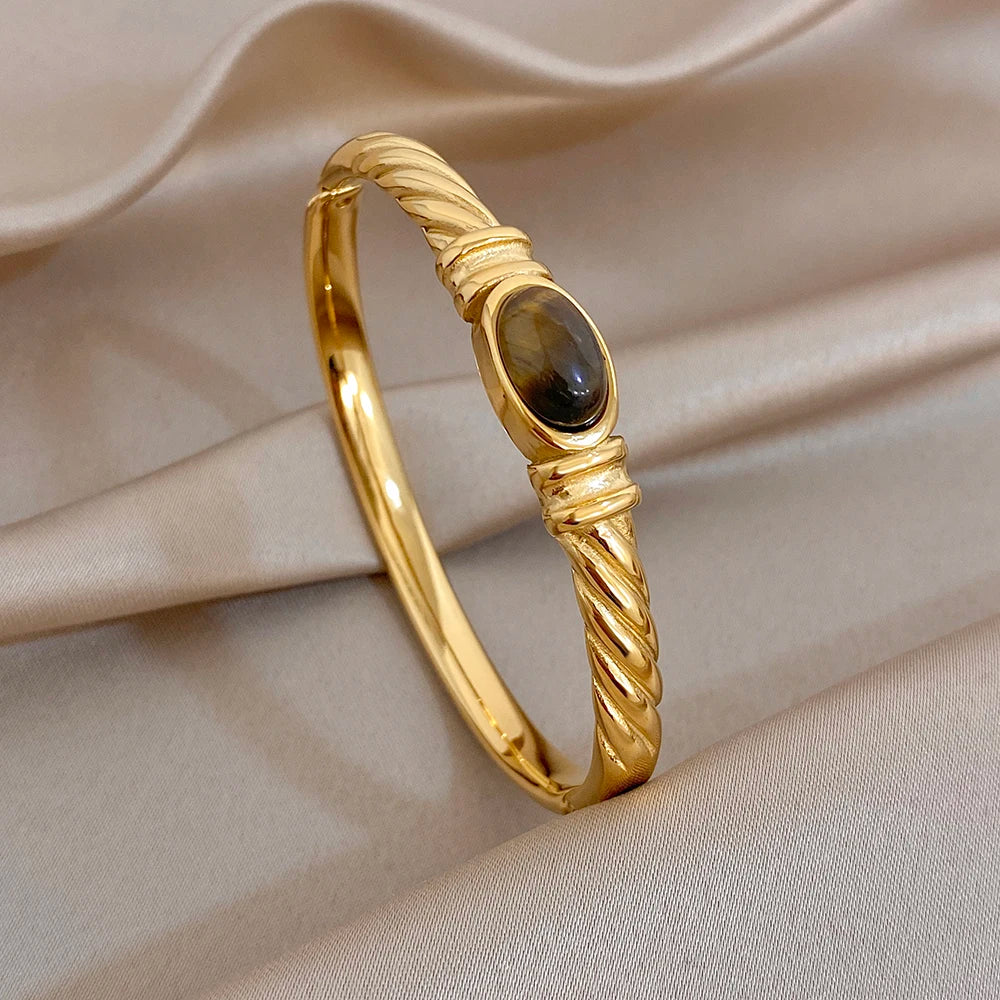 Gold-tone twisted cuff bangle with dark oval center stone