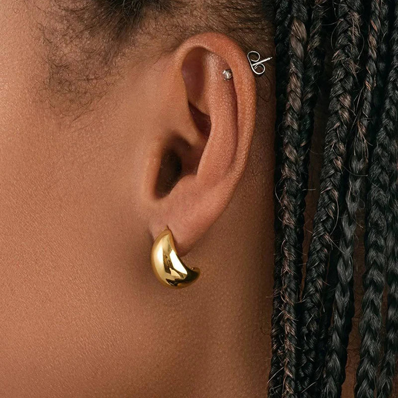 Gold-tone crescent-shaped dome hoop earring worn on an ear